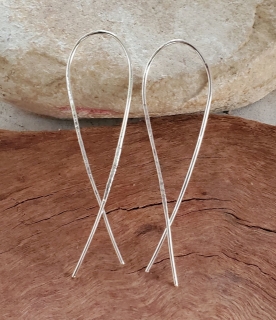Long silver arc earrings on rock