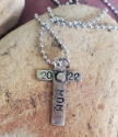 stamped message on silver riveted cross necklace on rock