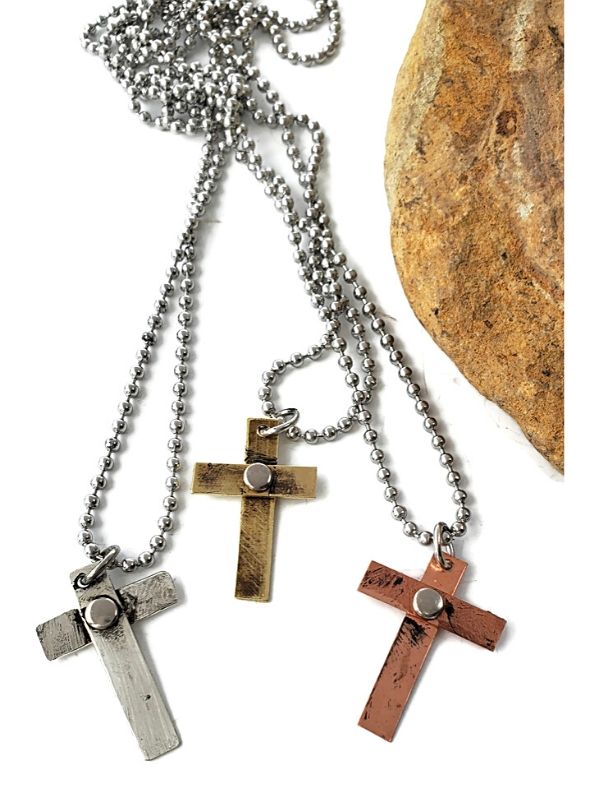 three handcrafted riveted mixed metal crosses necklaces  on rock